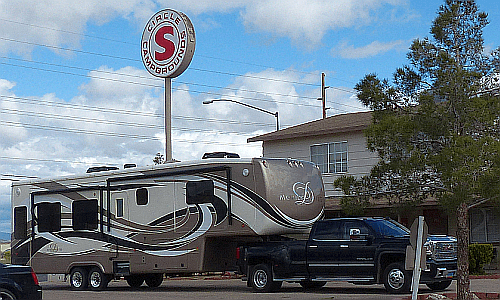 A fifth-wheel and pickup pulling in beneath the Circle S Campgrounds pole sign