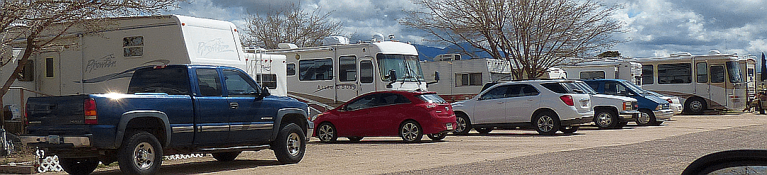 Rigs and vehicles parked along a campground row, with mountains on the horizon